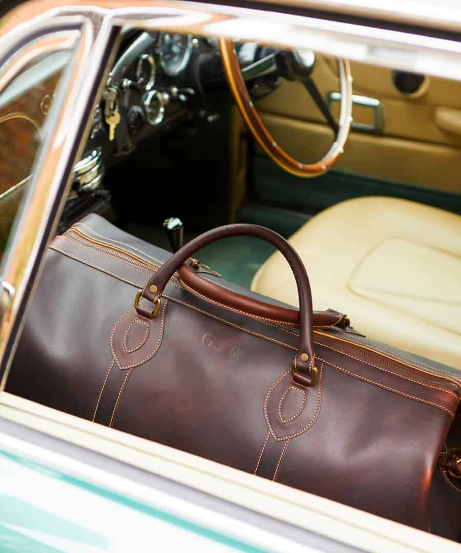 Luxury brown leather weekender bag sitting on the passenger seat of a car