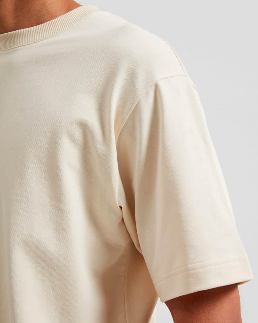 A close up of an off-white men's heavyweight T-shirt, focusing on the neck line and sleeve