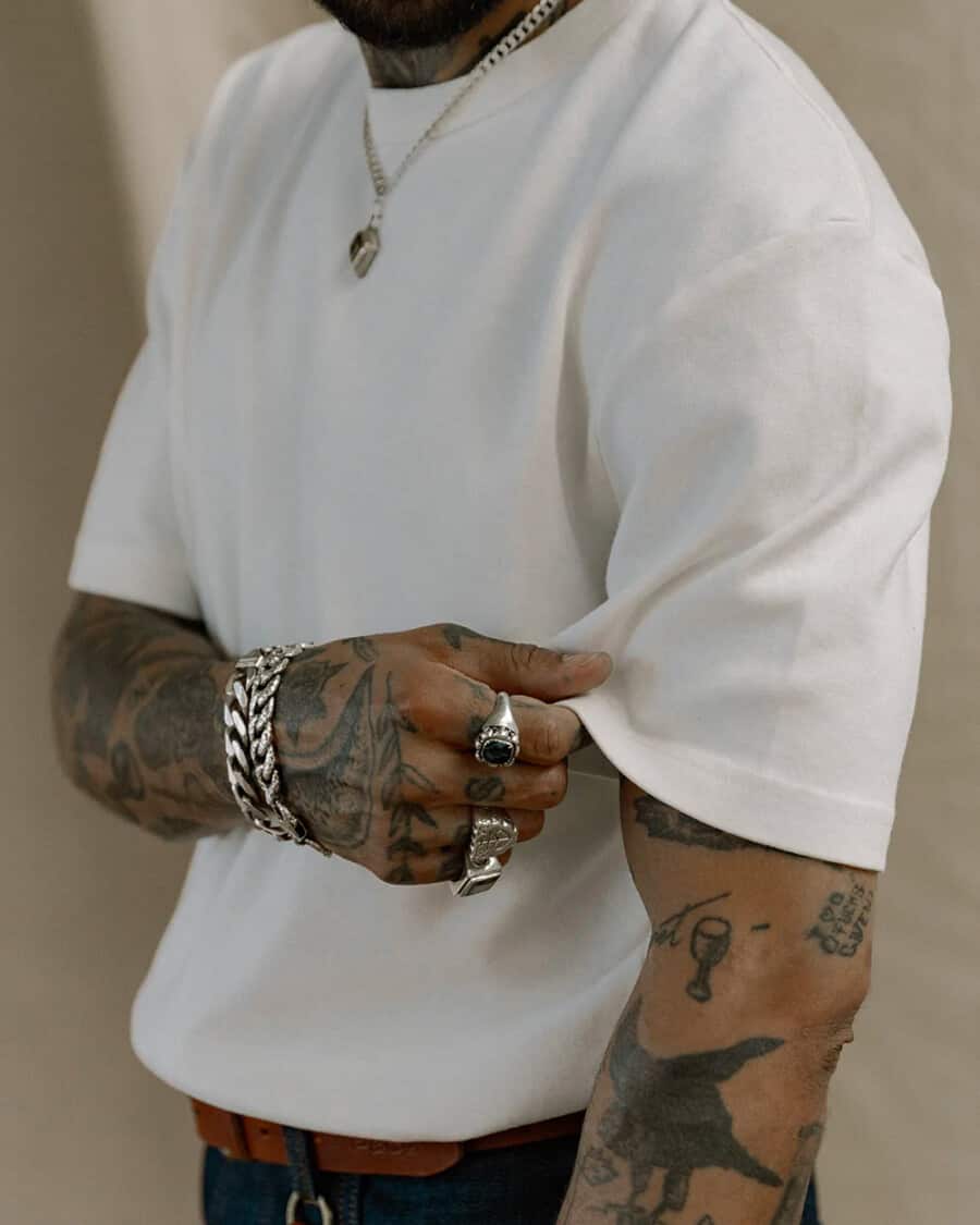 A man wearing a thick, heavyweight white T-shirt with jeans and chunky jewellery
