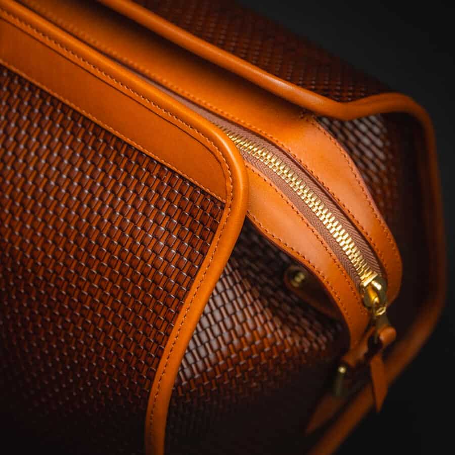 A close up of a luxurious brown woven leather weekender bag with gold hardware by Frank Clegg