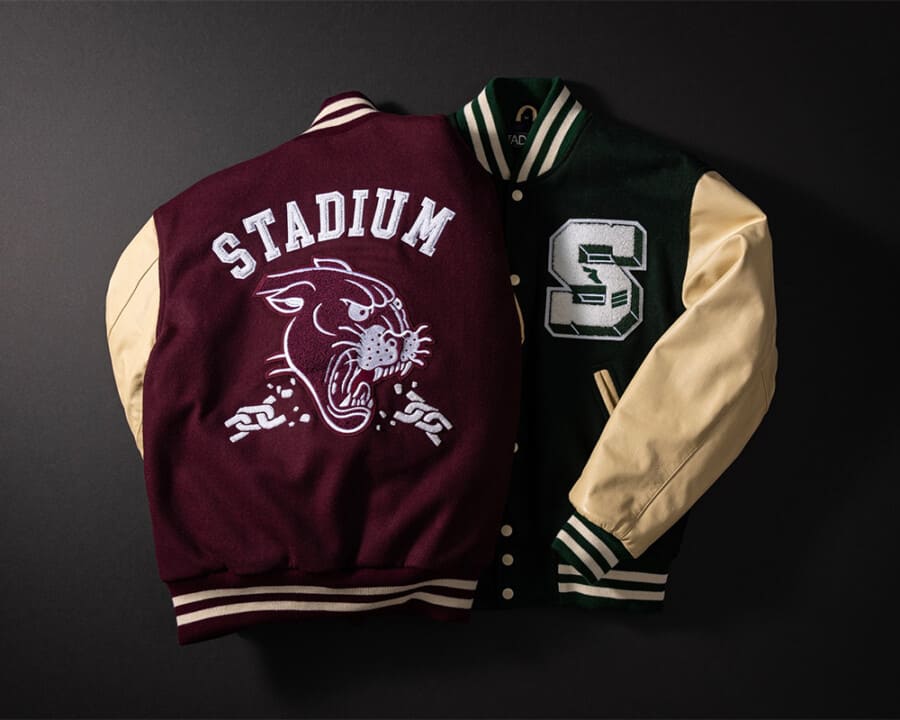 Two classic men's varsity jackets laid over each other in burgundy/cream and dark green/cream