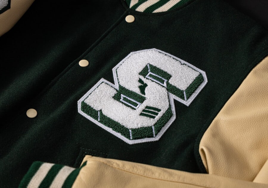 Close up of a classic men's varsity jacket in green and cream with an S patch logo to the chest