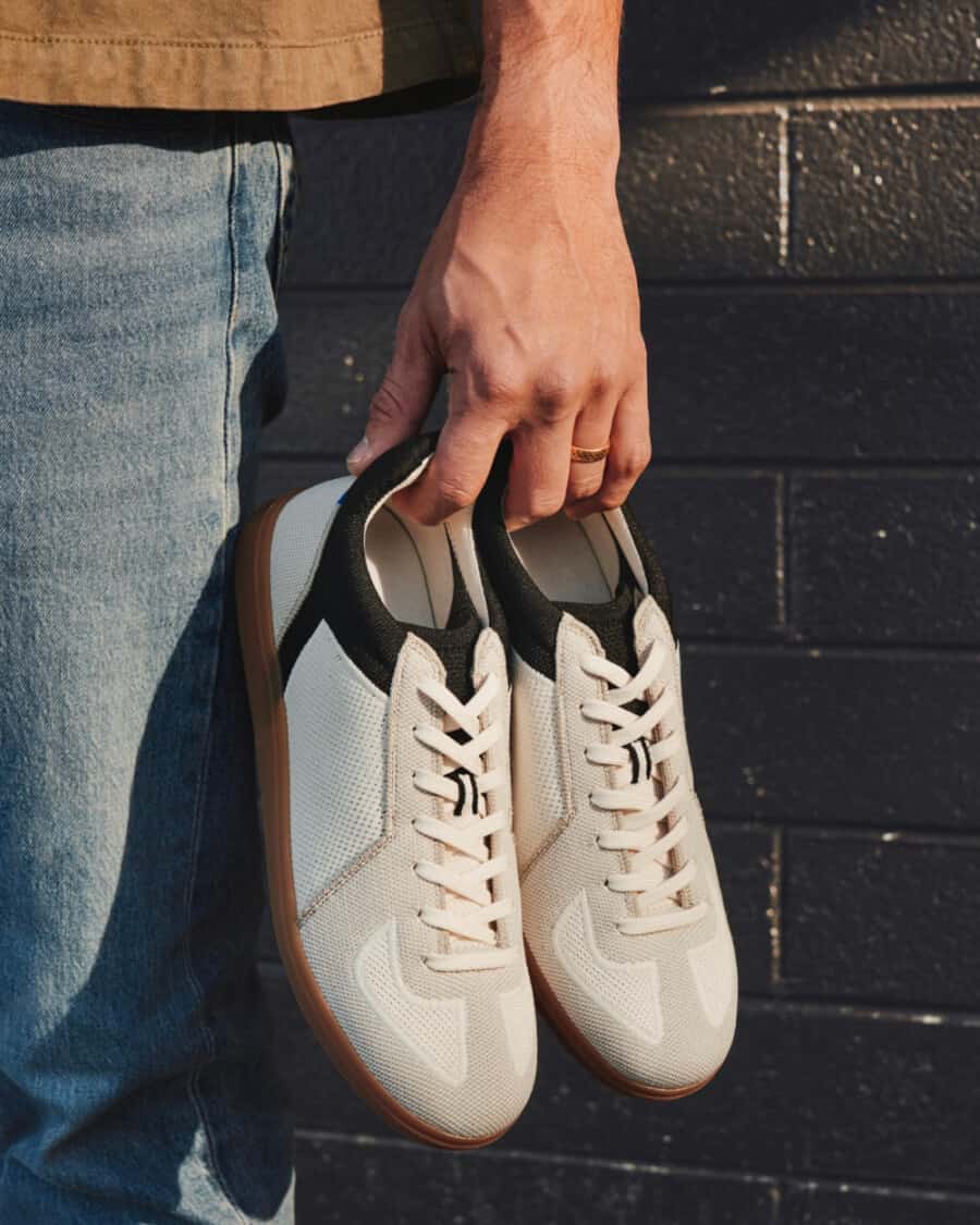 Man holding a pair of white Rothy’s RS01 sneakers