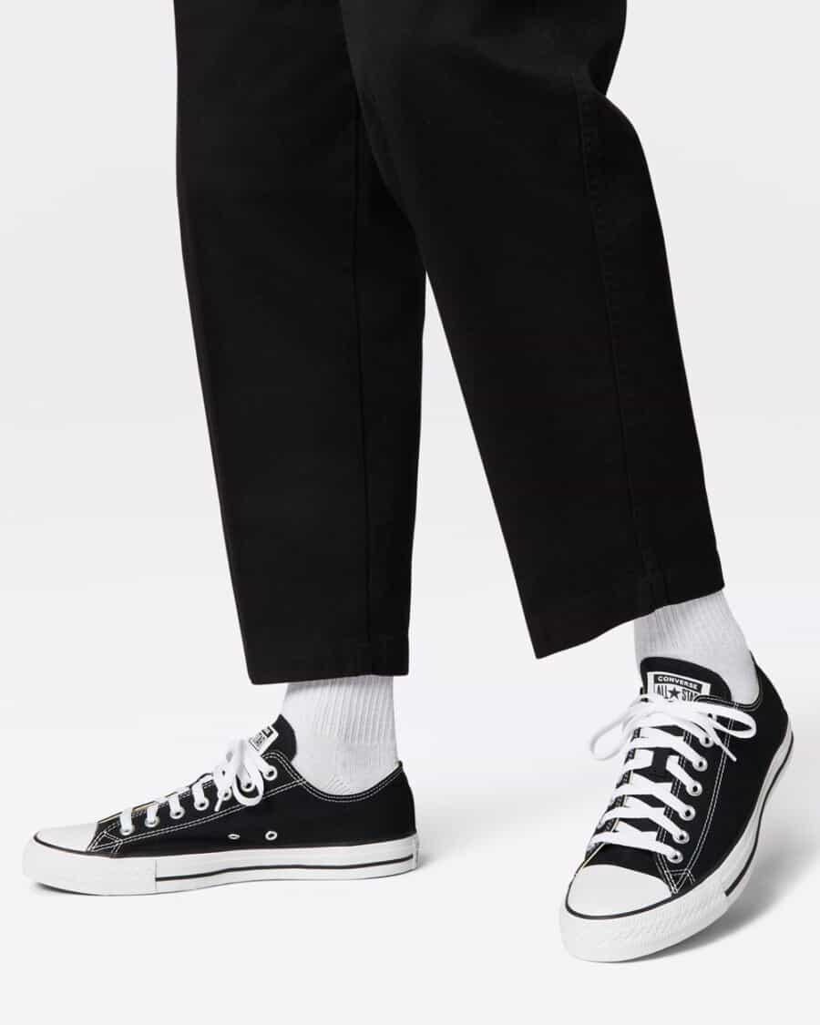 Man wearing a pair of low top black canvas Converse All Stars with black cropped pants and white socks