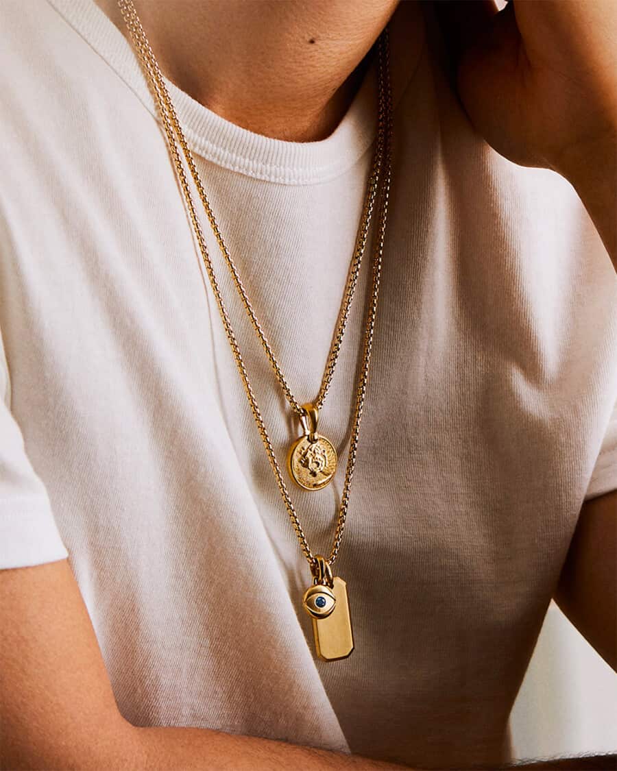 Man wearing white T-shirt with two gold pendant necklaces layered over the top