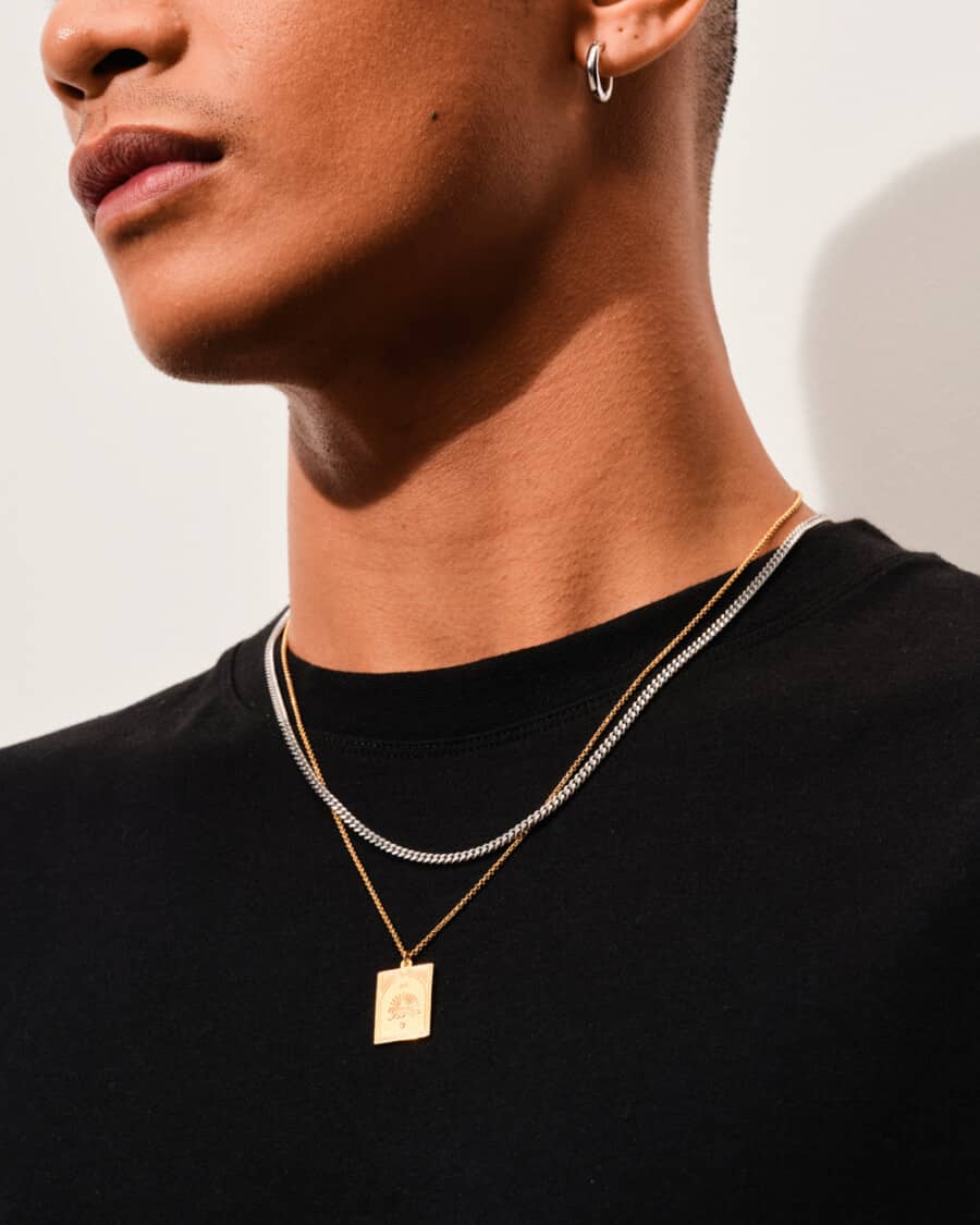 Man wearing a black T-shirt with a silver chain necklace and a gold pendant necklace over the top