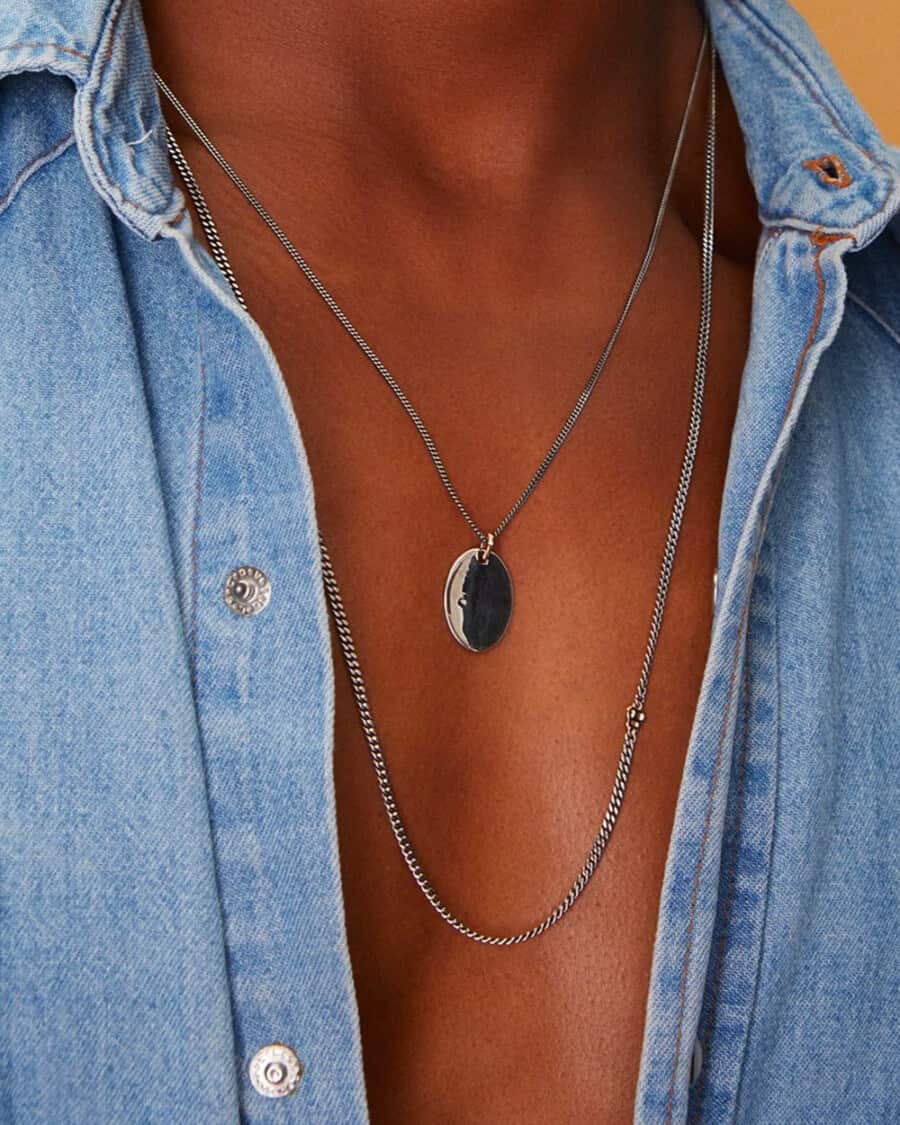 Man wearing unbuttoned denim shirt with two different silver chain necklaces on