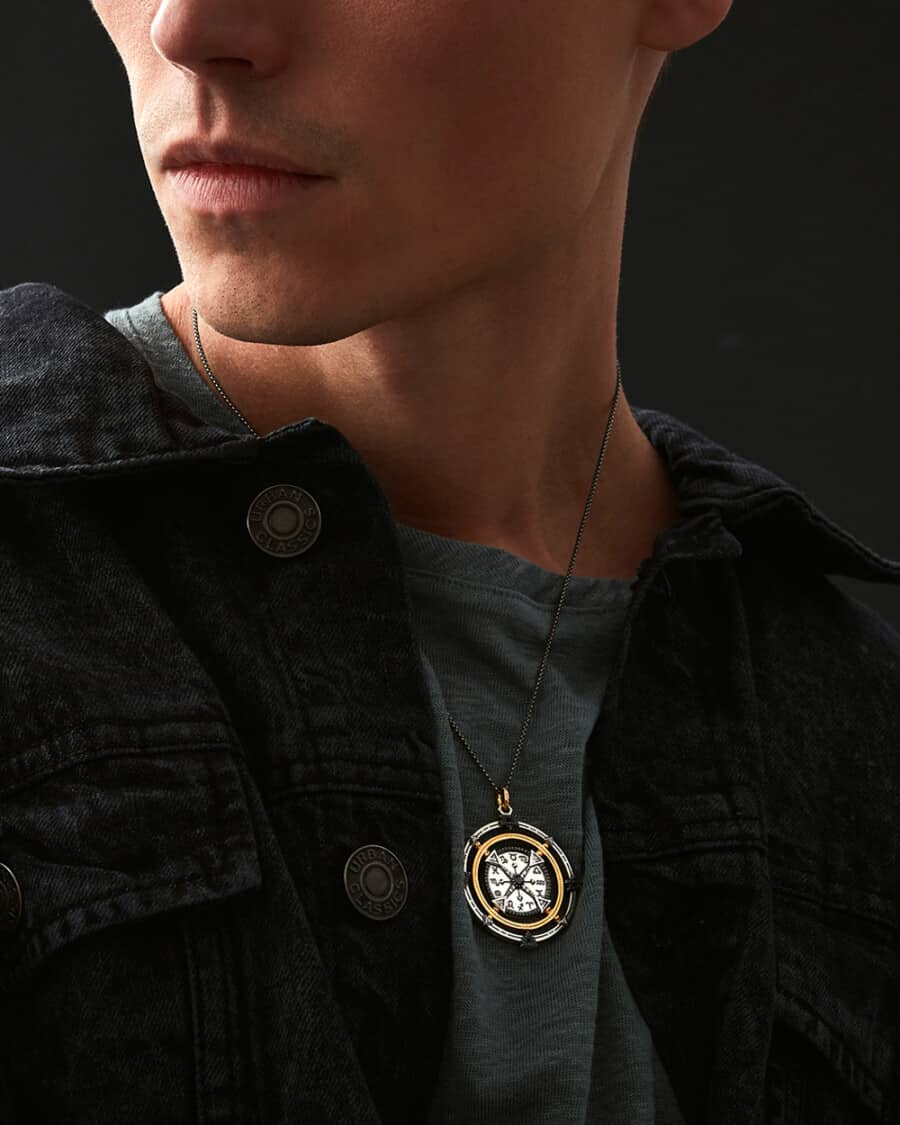 Man wearing grey T-shirt and black denim jacket with a large pendant chain necklace over the top