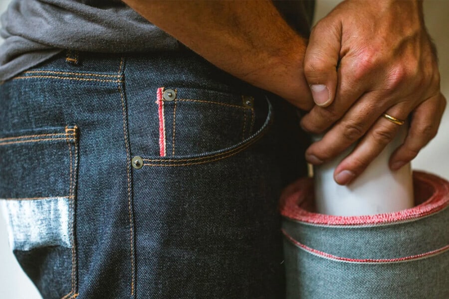 A close up of a man wearing Raleigh Denim Workshop Made in USA jeans holding a roll of selvedge edge