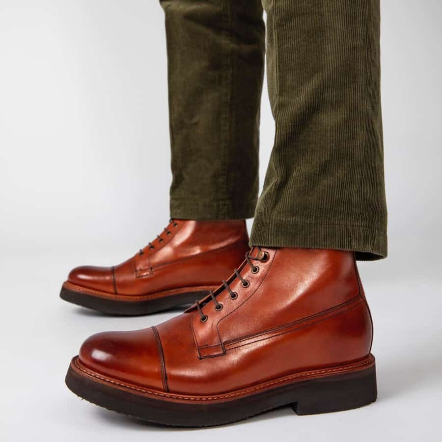 A pair of brown leather Derby boots with a thick rubber sole for height worn with green corduroy trousers