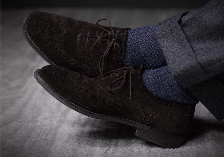 Men's suede brown business casual brogue shoes worn with grey tailored trousers and dark blue socks