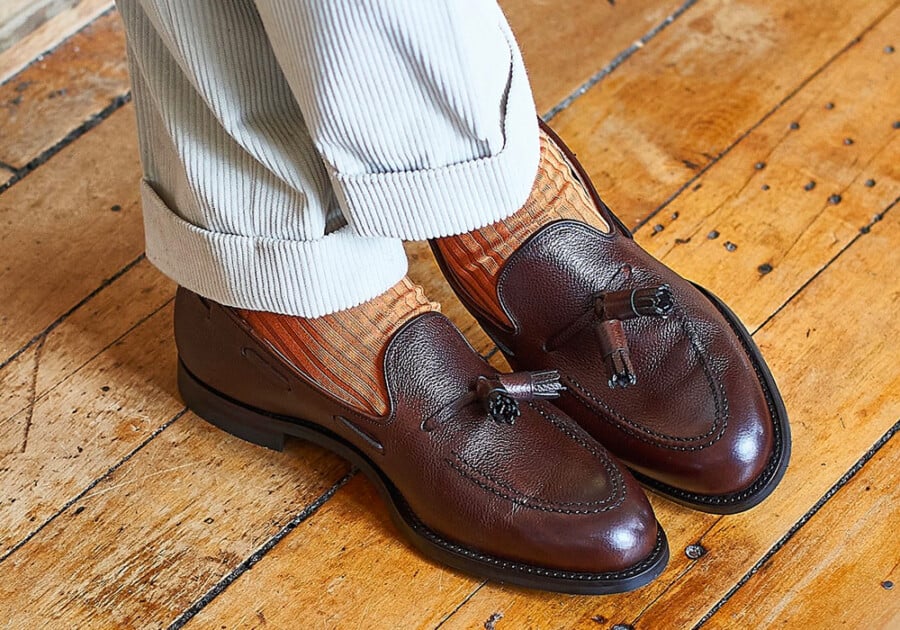Men's brown leather business casual tassel loafers worn with off-white corduroy trousers and orange socks
