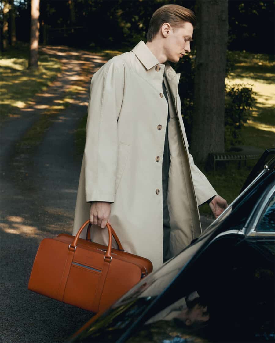 Man carrying a luxury tan leather Carl Friedrik weekender bag