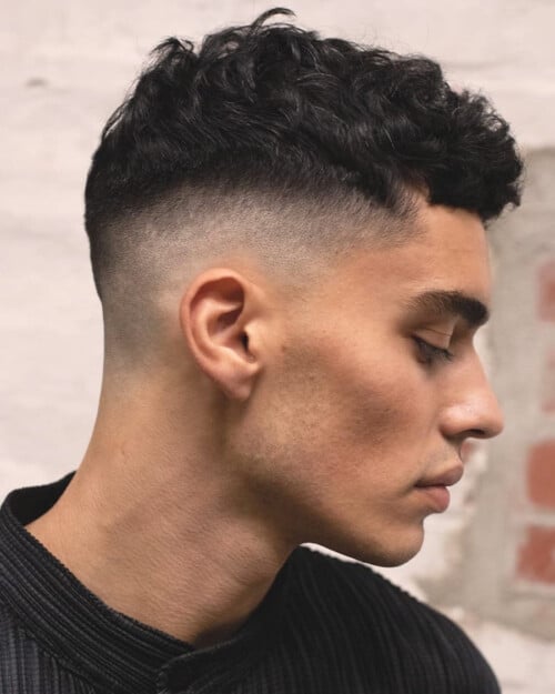 Man with a short curly hair French crop haircut and high skin fade