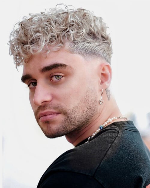 Man with bleached white/blonde curly hair with a French crop and low skin fade