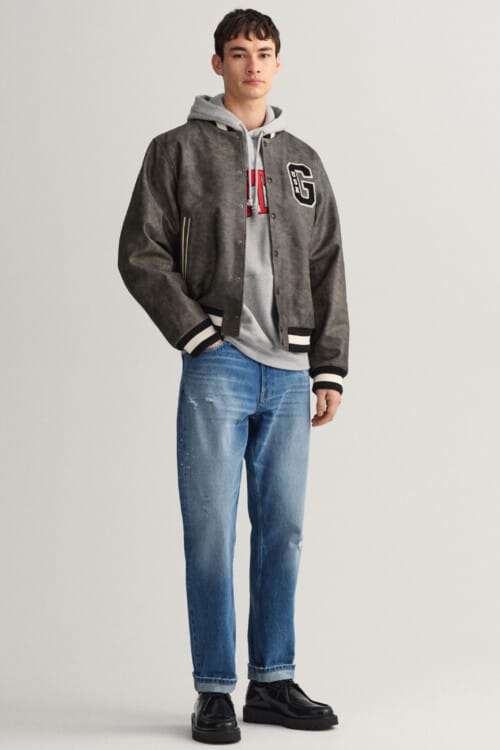 Men's mid wash jeans, grey hoodie, leather varsity jacket and black shoes outfit