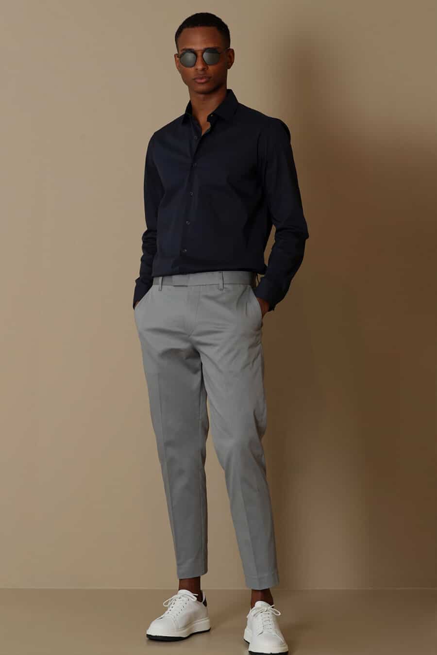 Men's cropped grey pants, black tucked in shirt and white sneakers outfit