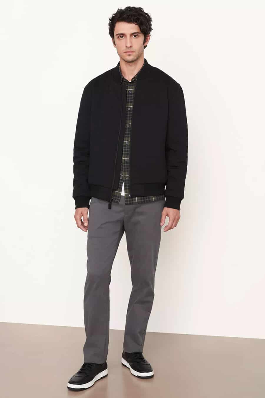 Men's dark grey chinos, green checked flannel shirt, black bomber jacket and black sneakers outfit