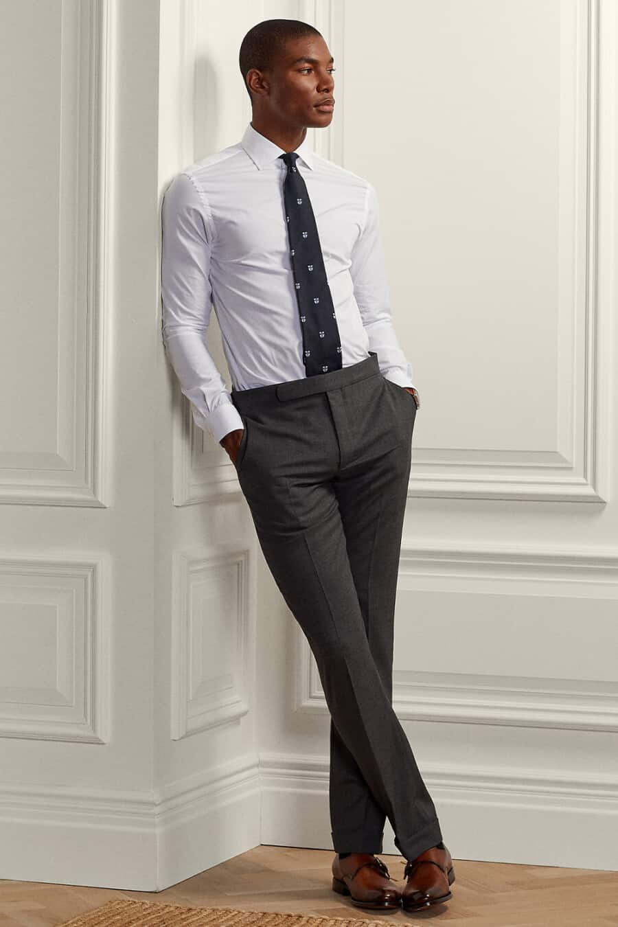 Men's grey dress pants, white shirt, patterned navy tie and brown monk strap shoes outfit