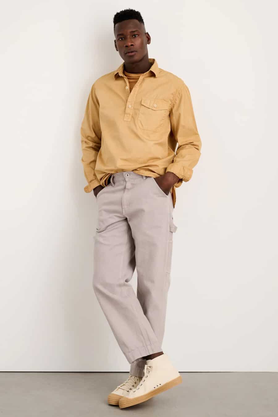 Men's light grey carpenter pants, yellow popover shirt and cream canvas high tops outfit