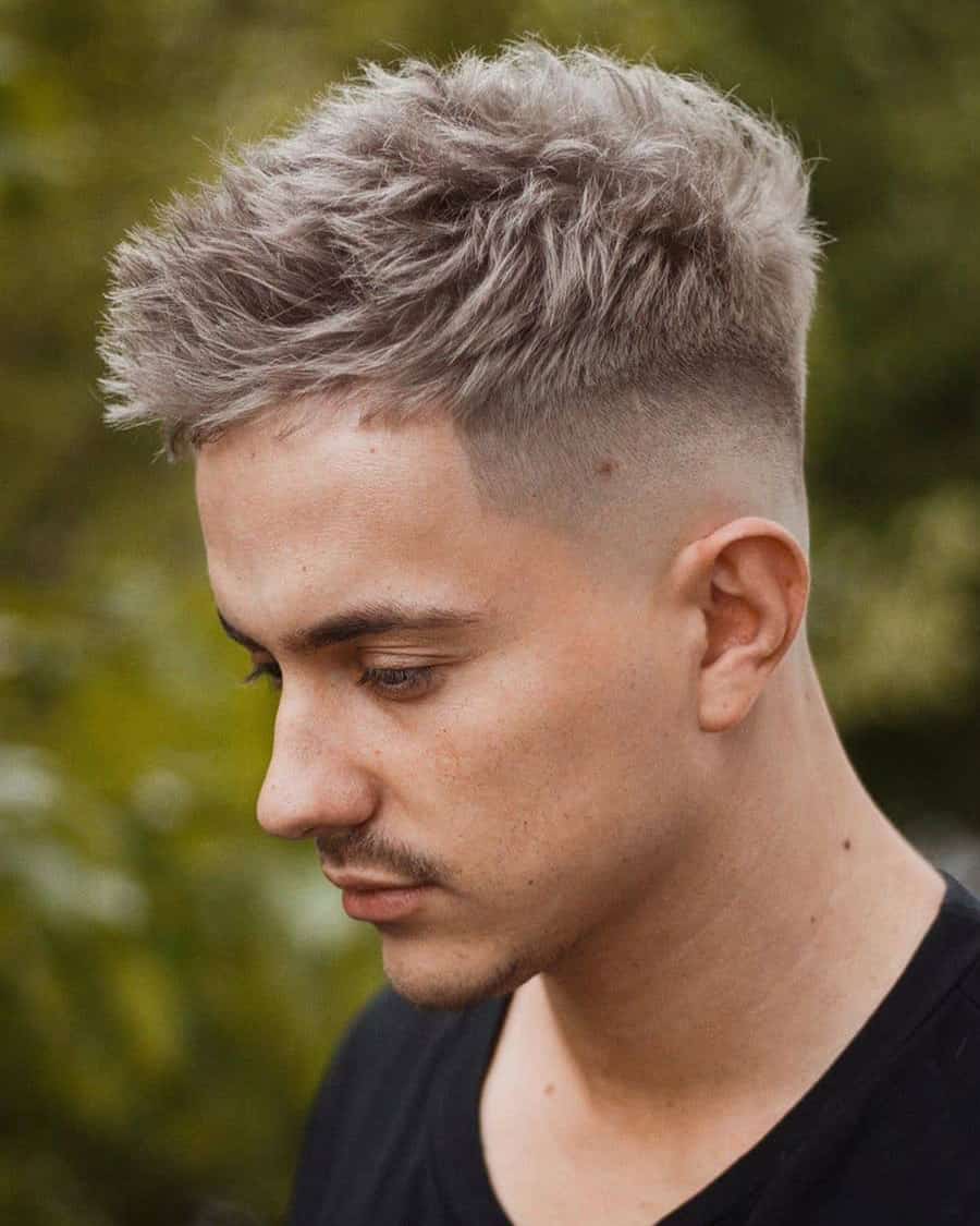 Men's short messy haircut with blonde highlights and a high taper fade