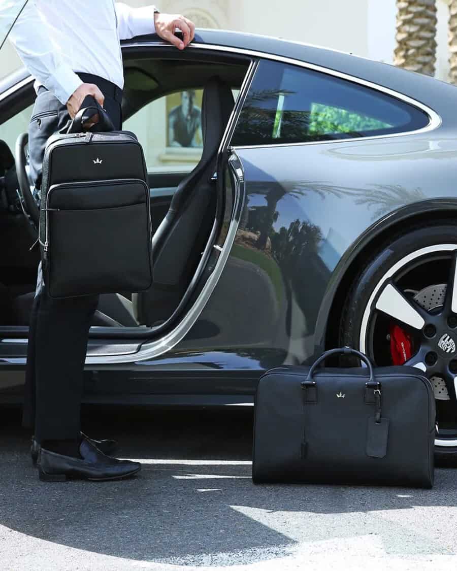 A luxury Roderer black leather backpack and holdall in front of a Porsche
