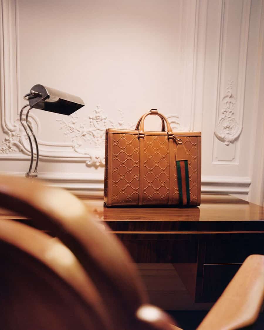 Luxury tan leather embossed Gucci tote bag set on a wooden desk