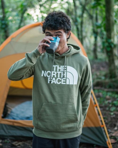 Man wearing a green logo North Face hoodie drinking a drink outdoors
