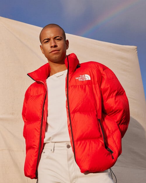 Man wearing a bright red North Face padded down jacket, white T-shirt and stone chinos