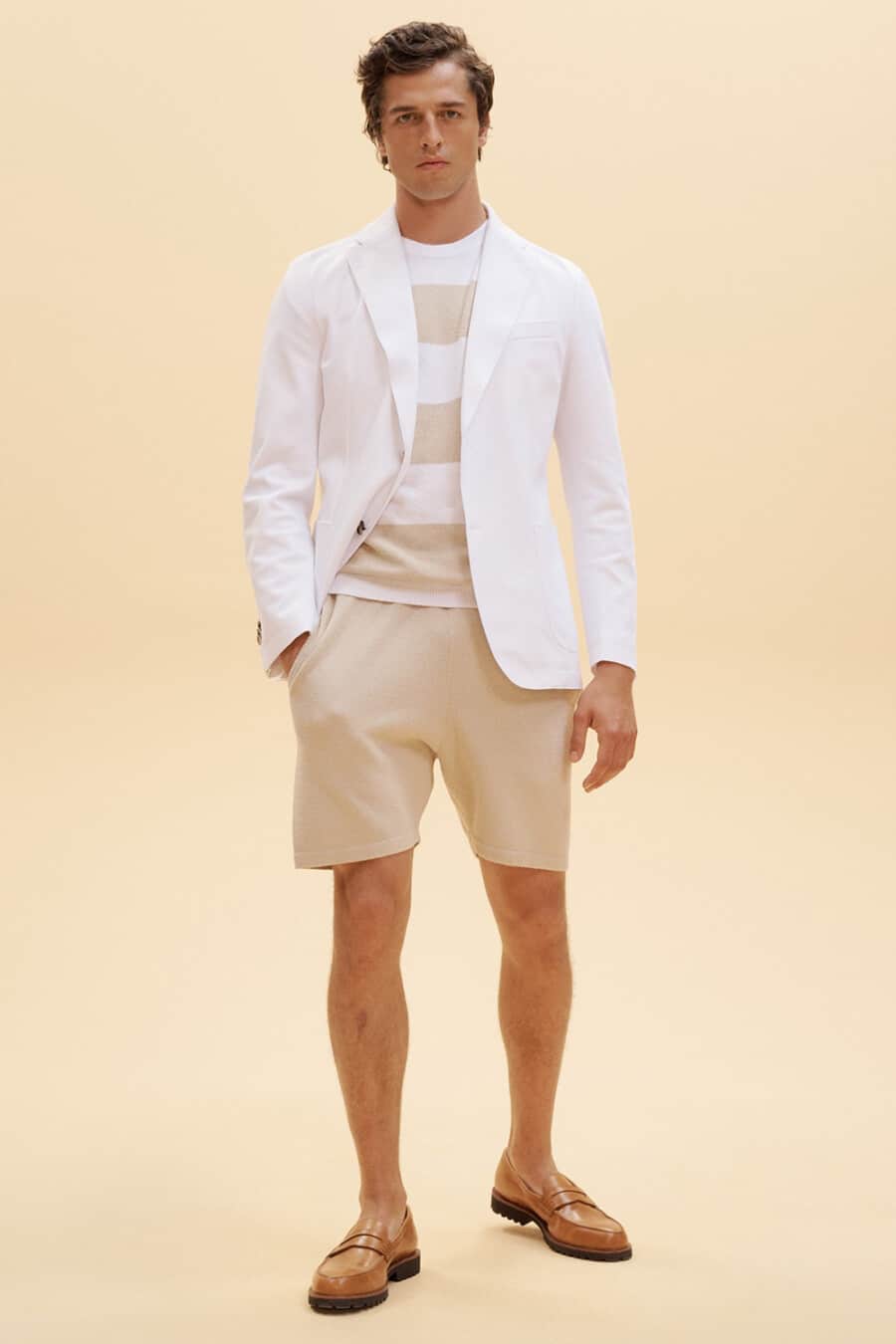 Men's beige tailored shorts, white and beige striped T-shirt, white blazer and tan leather penny loafers outfit