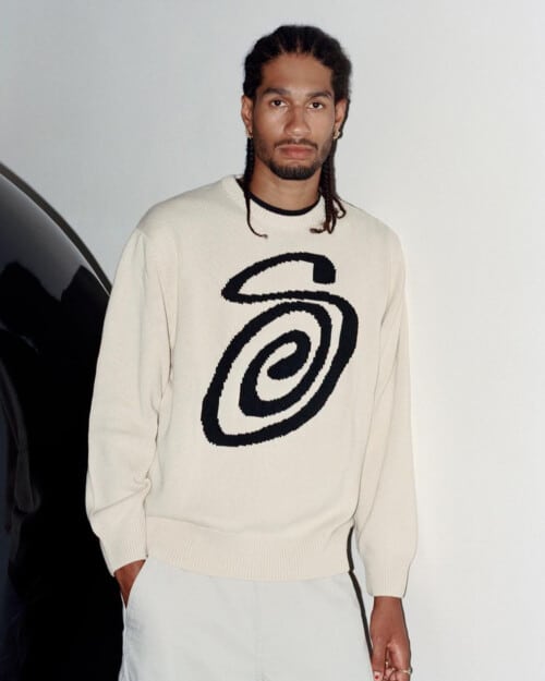 Man wearing relaxed white Stussy sweater with S on the front