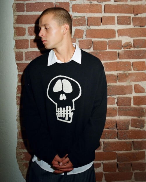 Man wearing relaxed black Stussy sweater with skull to front