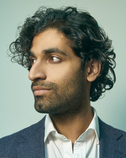 Indian man with mid-length black wavy hair in loose side parting