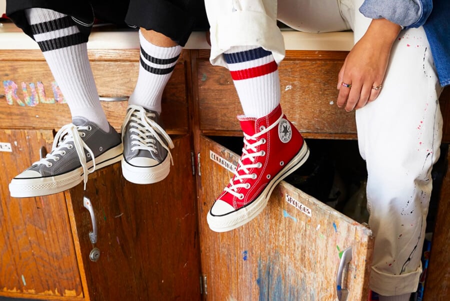 Grey Converse Chuck Taylor low and bright red Converse Chuck Taylor Hi sneakers worn on feet with long white sports socks