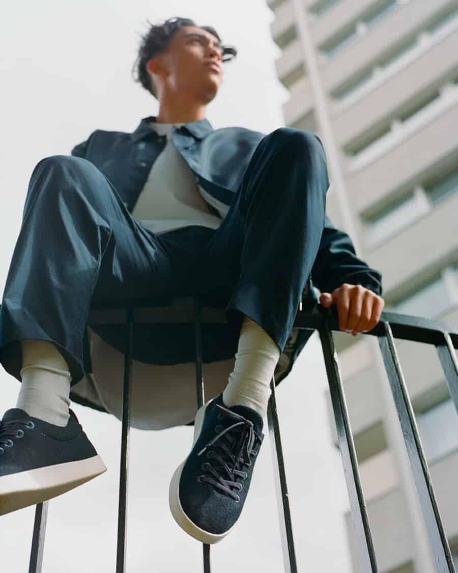 Man sitting on railing wearing affordable knitted sneakers by AllBirds