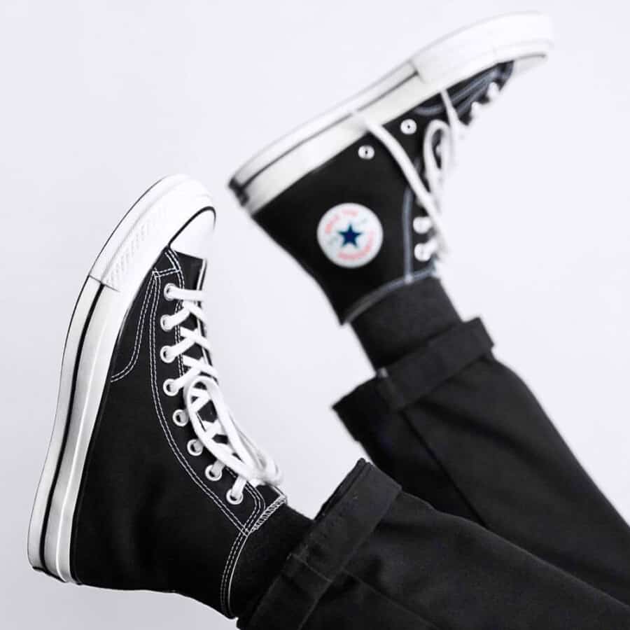 A pair of cheap Converse Chuck Taylor Hi black canvas sneakers on feet worn with black pants