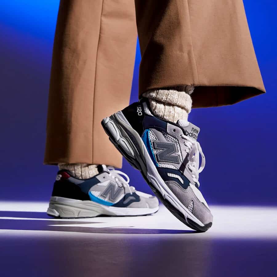 A pair of grey and navy New Balance sneakers made in the USA worn with khaki pants and beige wool socks