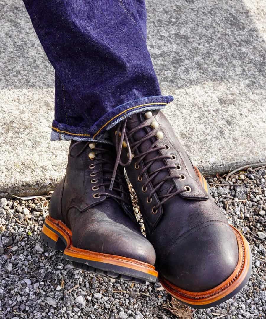 A pair of black leather made in the USA work boots worn on feet with raw denim jeans by Parkhurst Boots