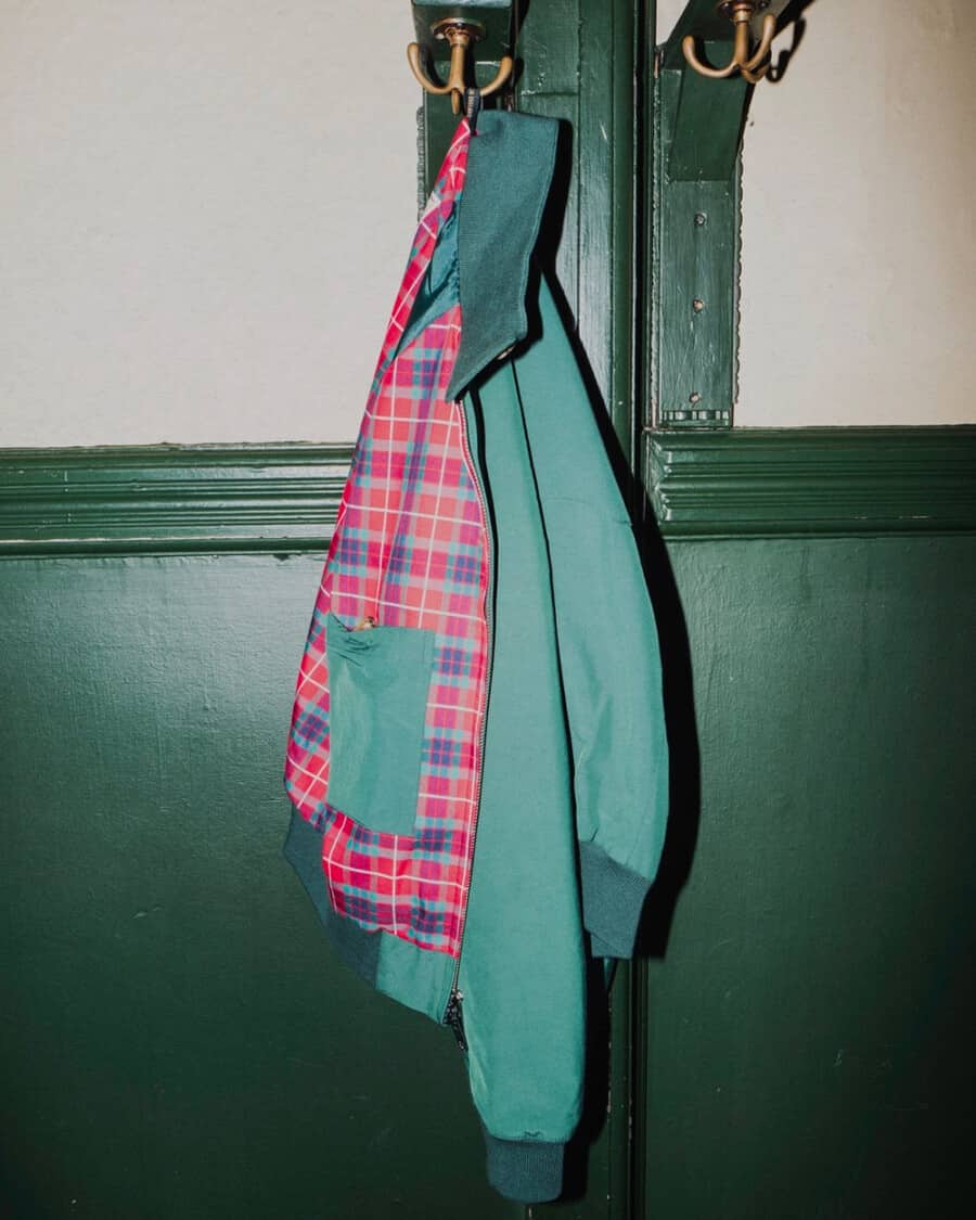 Men's green Baracuta Harrington jacket with red tartan lining hung up on a coat peg
