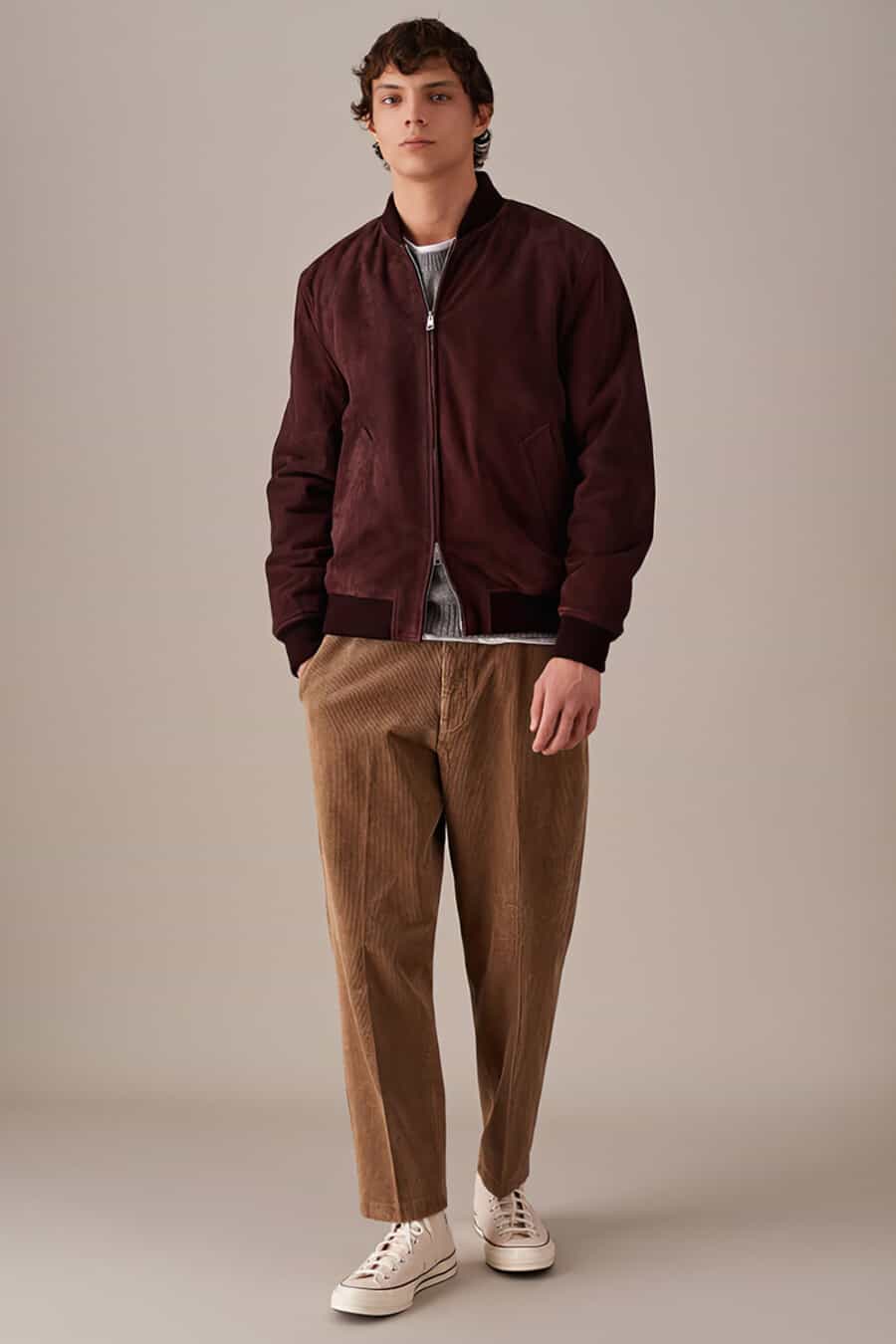 Men's brown corduroy trousers, white T-shirt, grey sweater, burgundy suede bomber jacket and white Converse high top sneakers outfit