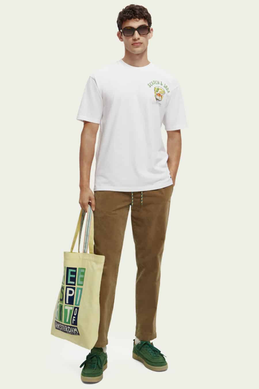 Men's brown pants, white graphic T-shirt, green sneakers and tote bag outfit