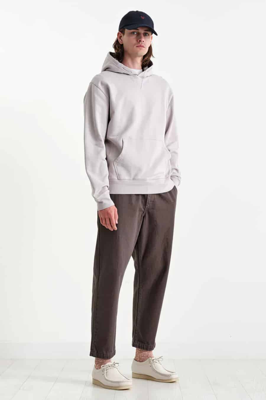 Men's dark brown pants, white Wallabee shoes, grey hoodie and navy baseball cap outfit
