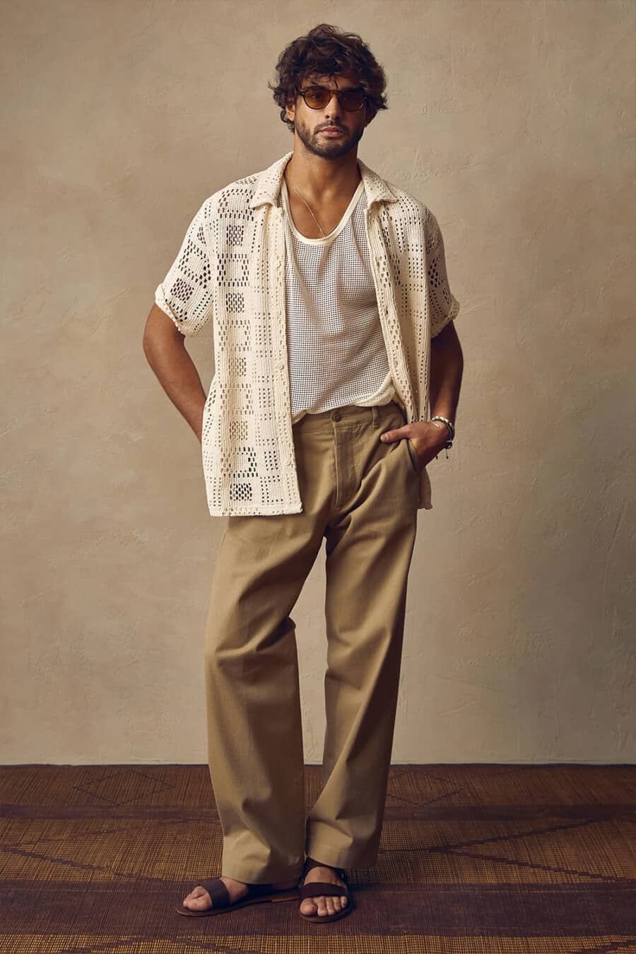 Men's loose brown pants, off-white knitted vest, crochet white short sleeve shirt and brown leather sandals outfit