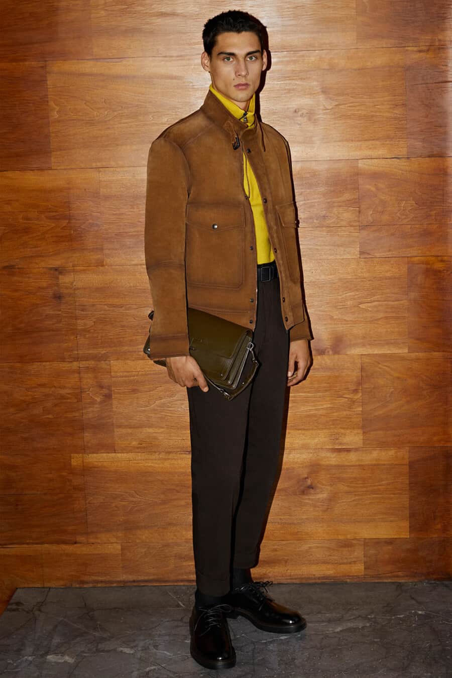 Men's dark brown pants, bright yellow funnel neck sweater, tan suede jacket, brown leather shoes and green leather bag outfit