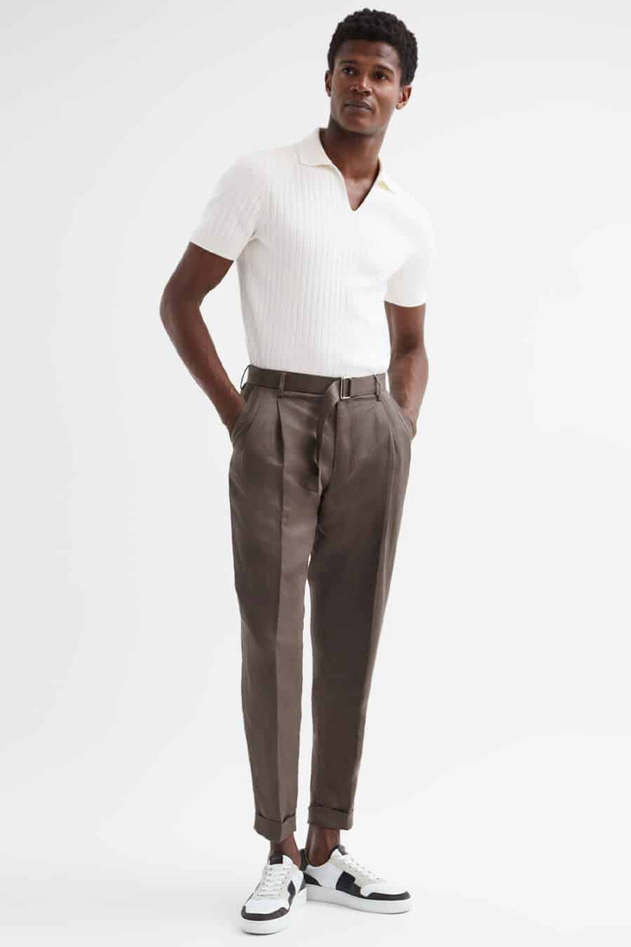 Men's brown pleated trousers, tucked in white polo shirt and white sneakers outfit