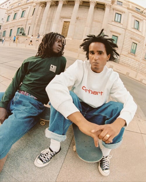 Two men wearing mid-wash jeans and Carhartt WIP sweatshirts in white and green