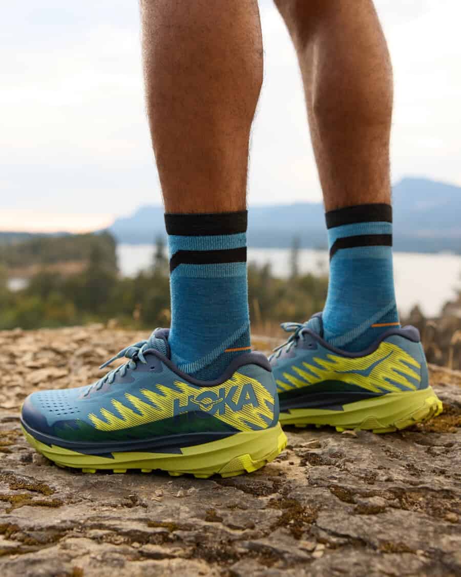 Men's HOKA trail running shoes worn on feet with blue socks