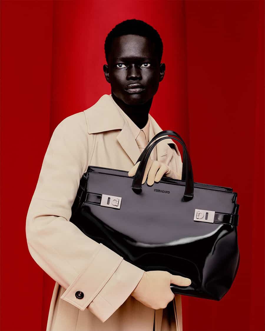 Black man holding a patent leather luxury tote bag by Ferragamo