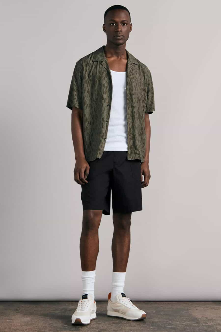 Men's black cotton shorts, white tank top vest, white tube socks, cream running sneakers and printed green Cuban collar shirt outfit