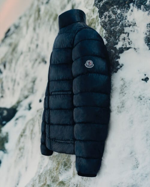 A black men's luxury Moncler puffer jacket on a rock covered with snow